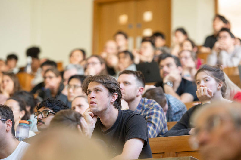 Audience listening attentively, leaning forward, some with chins on hands