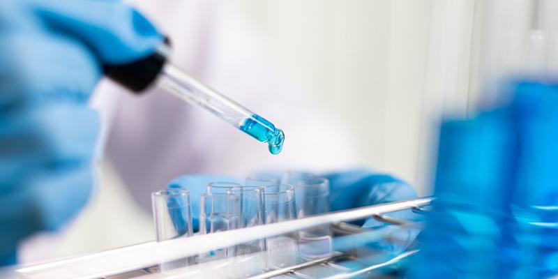 A Photo of a scientist dropping blue chemical into test tubes