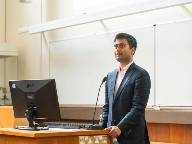 Dr Navoneel Sen standing by a lecturn, smiling, as he gives a lecture during the 5th birthday symposium held by Oxford's Kavli Institute for Nanoscience Discovery (Kavli INsD)