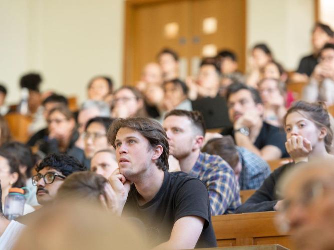 Audience listening attentively, leaning forward, some with chins on hands