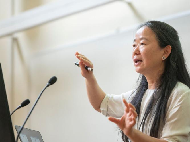 Side view of head and shoulders of Professor Jue Chen presenting at the Kavli Oxford Lecture Award, describing something with hand gestures.