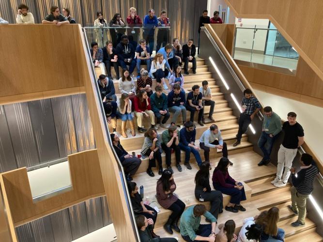 Kavli Oxford researchers listening to presentations while standing and sitting on the main stairway