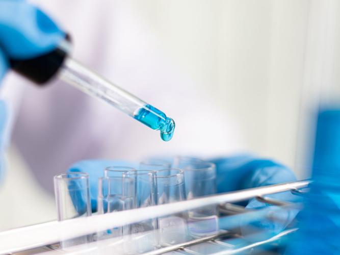 A Photo of a scientist dropping blue chemical into test tubes