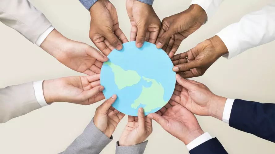 A photograph of hands of people from different racial backgrounds, holding a picture of the world together.