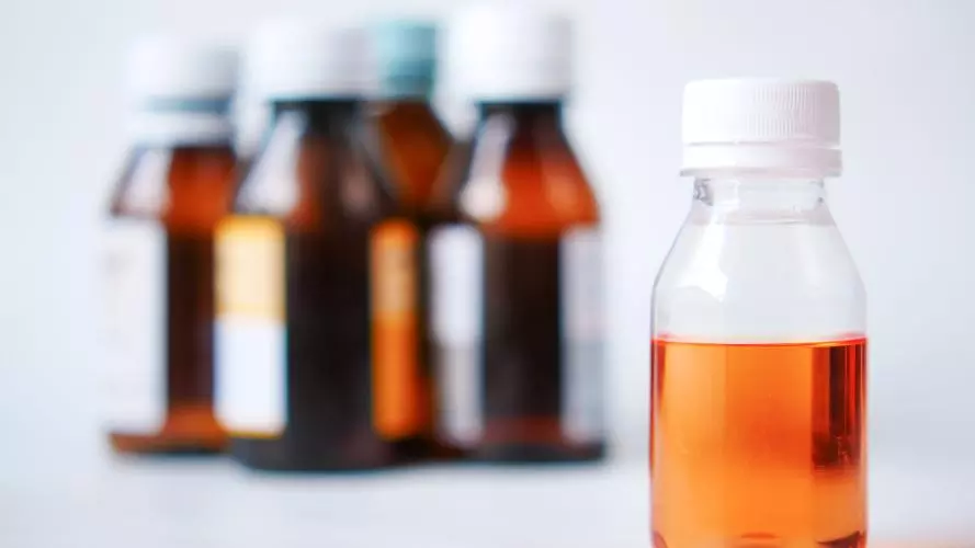 A group of medicine bottles with focus on one filled with orange syrup liquid.