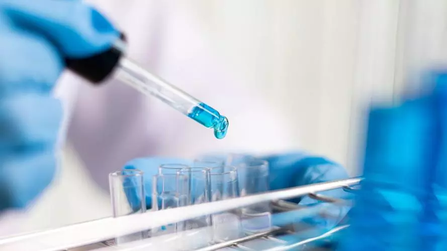 A Photo of a scientist dropping blue chemical into test tubes