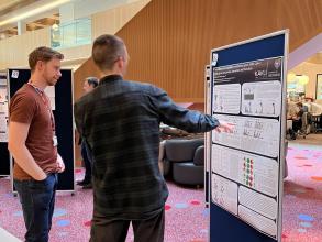 A photograph of Sean Burnap presenting his poster to a colleague. 