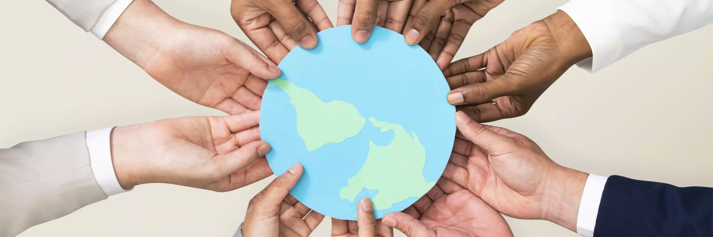 A photograph of hands of people from different racial backgrounds, holding a picture of the world together.